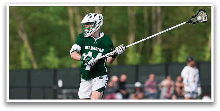 A man wearing a green and white uniform holding a lacrosse stick. Description generated by AI