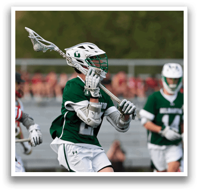 A man in a green shirt and white shorts is holding a lacrosse stick. Description generated by AI