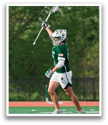 A man wearing a green and white uniform is holding a lacrosse stick. Description generated by AI