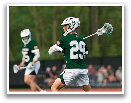 A man wearing a green shirt and white shorts is holding a lacrosse stick. Description generated by AI