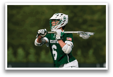 A man wearing a green and white uniform is holding a lacrosse stick. Description generated by AI