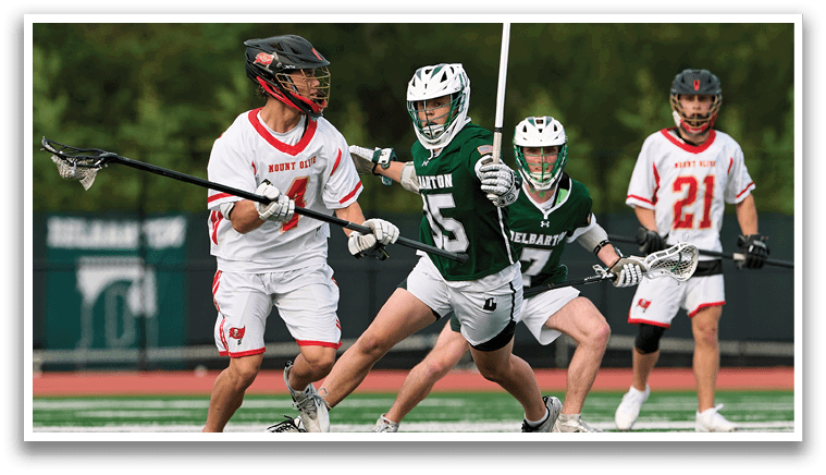A man wearing a green shirt and white shorts is holding a lacrosse stick. Description generated by AI