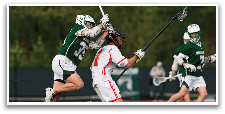 A man in a green shirt is running with a lacrosse stick. Description generated by AI