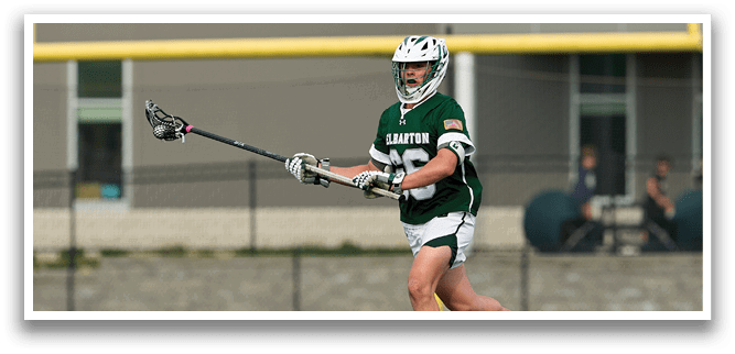 A woman wearing a green and white uniform is playing lacrosse. Description generated by AI