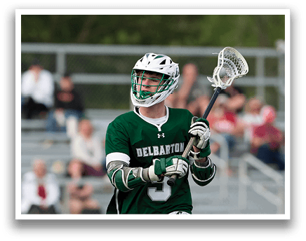 A man wearing a green and white shirt and shorts is holding a lacrosse stick. Description generated by AI