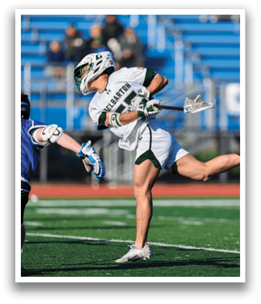 A man wearing a white and green shirt is holding a lacrosse stick. Description generated by AI