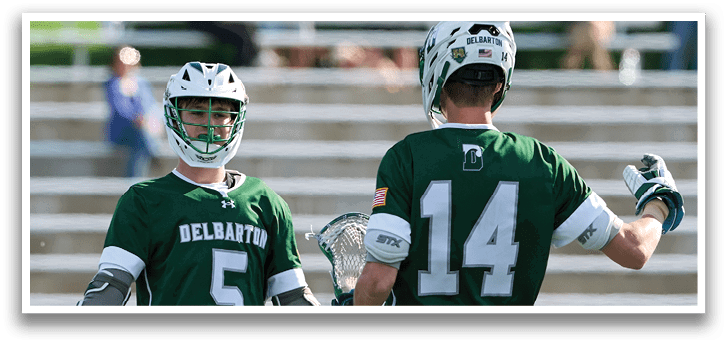 Two men wearing green jerseys and holding lacrosse sticks. Description generated by AI