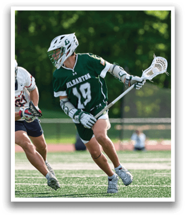 A man in a green shirt and white shorts is playing lacrosse. Description generated by AI