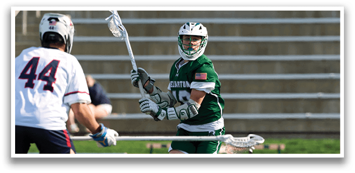 A man wearing a green and white uniform is holding a lacrosse stick. Description generated by AI