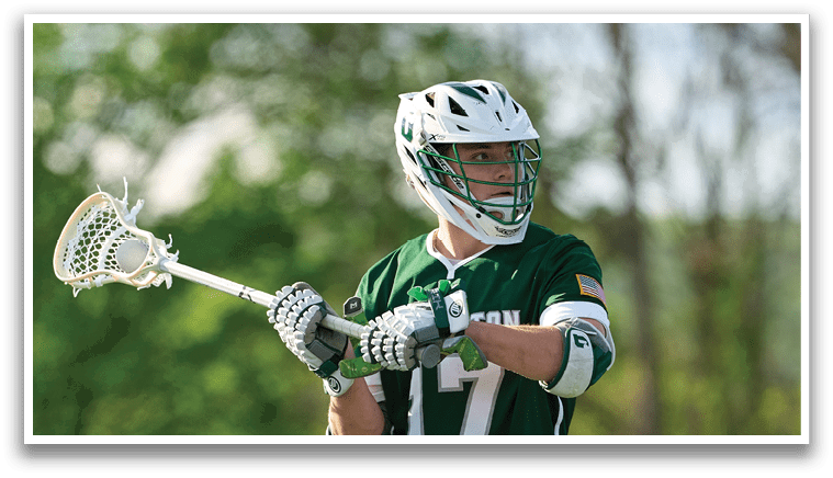 A man wearing a green and white jersey holding a lacrosse stick. Description generated by AI