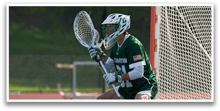 A man wearing a green and white uniform is crouching in front of a net. Description generated by AI