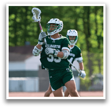 A man in a green jersey is holding a lacrosse stick. Description generated by AI