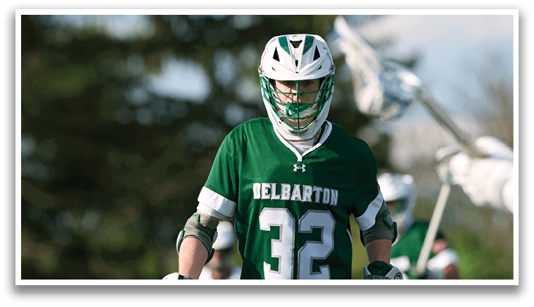 A man wearing a green and white shirt and holding a lacrosse stick. Description generated by AI