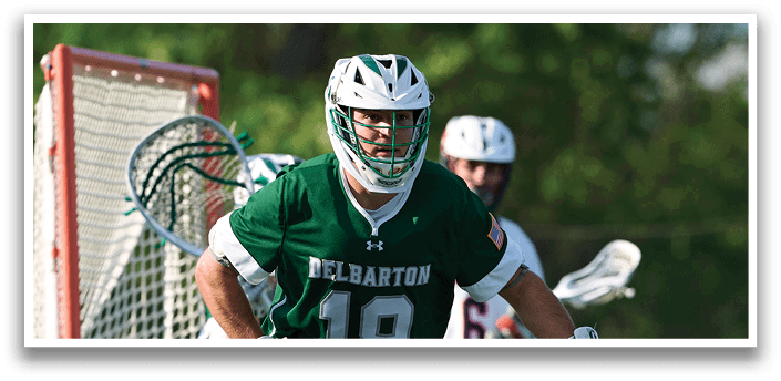 A man wearing a green and white uniform is holding a stick and playing lacrosse. Description generated by AI