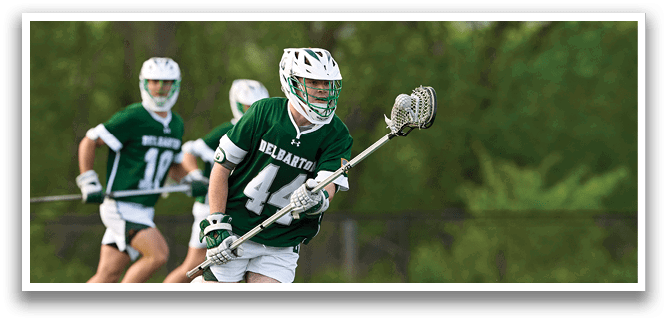 A man in a green and white uniform is running with a lacrosse stick. Description generated by AI