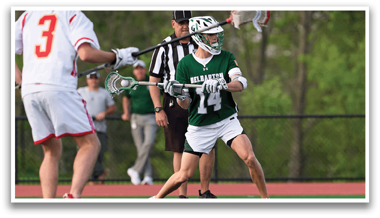 A man in a green shirt and white shorts is holding a lacrosse stick. Description generated by AI