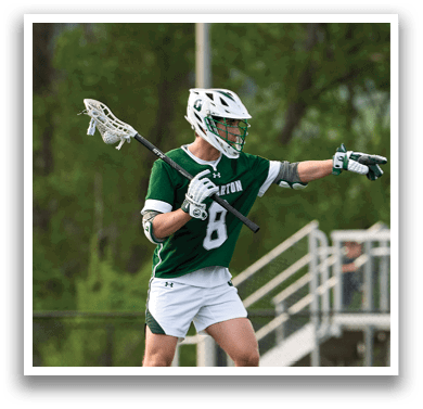 A man wearing a green and white jersey is holding a lacrosse stick. Description generated by AI