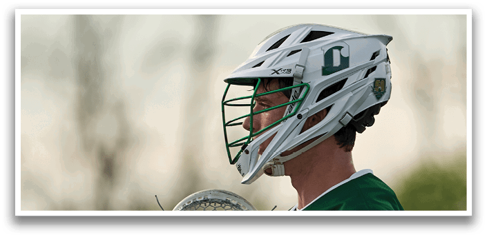 A man wearing a green shirt and white gloves holding a lacrosse stick. Description generated by AI
