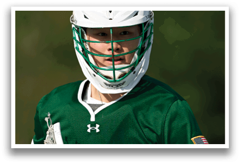 A man wearing a green and white jersey holding a lacrosse stick. Description generated by AI