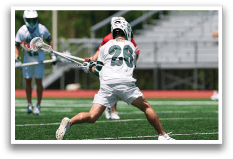 A man in a white shirt and green shorts is holding a lacrosse stick. Description generated by AI