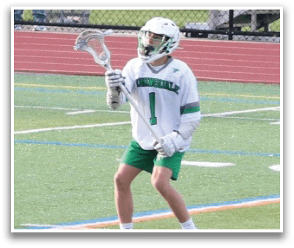 A young man wearing a white jersey and green shorts is holding a lacrosse stick and standing on a field. AI generated content