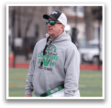 A man wearing a gray hoodie and black pants stands on a football field. He is holding a clipboard in his hand. AI generated content