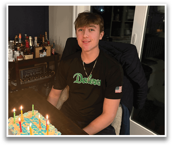 A young man is sitting at a table with a cake with candles in front of him. AI generated content