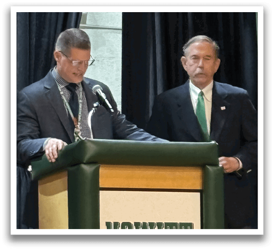A man giving a speech at a podium with a sign that says Howitt Middle School. Description generated by AI