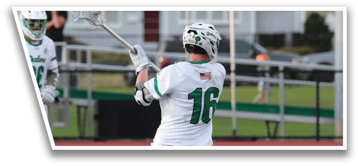 A man in a white and green uniform is holding a lacrosse stick and getting ready to hit a ball. Description generated by AI
