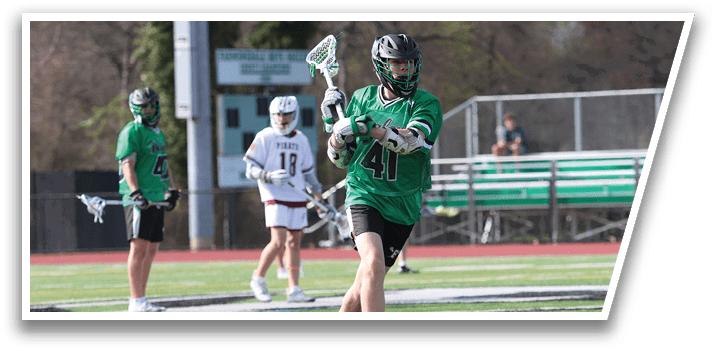 A man in a green shirt and white shorts holding a lacrosse stick. Description generated by AI
