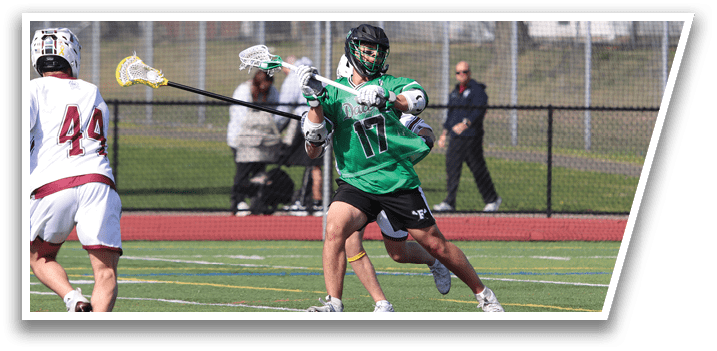 A man in a green shirt and black shorts is holding a lacrosse stick. Description generated by AI