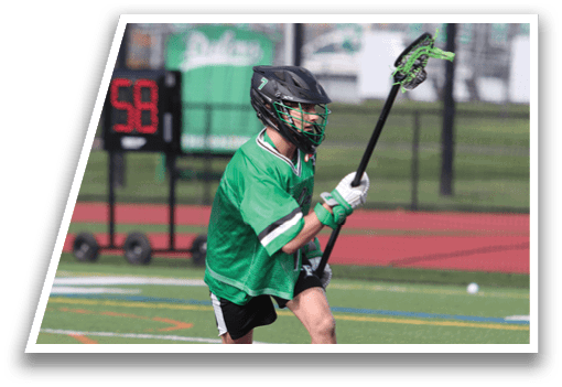 A boy in a green shirt and black shorts is holding a lacrosse stick. Description generated by AI