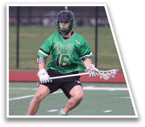 A man wearing a green shirt and white shorts is holding a lacrosse stick. Description generated by AI
