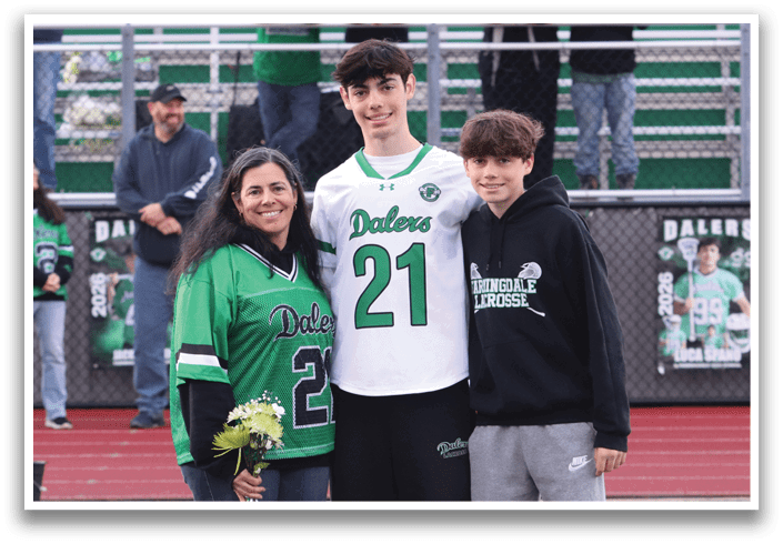 A man and woman standing on a football field with a boy in a green jersey. Description generated by AI