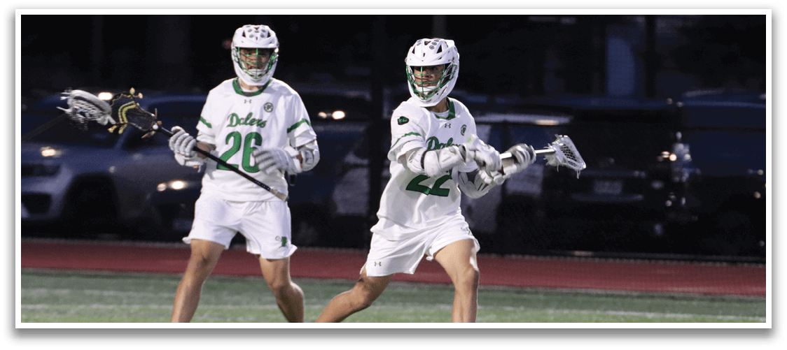 Two men playing lacrosse on a field. Description generated by AI