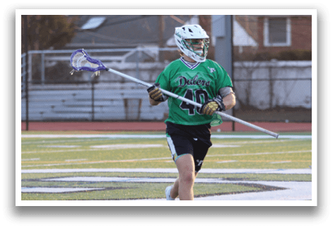 A man in a green shirt and black shorts holding a lacrosse stick. Description generated by AI