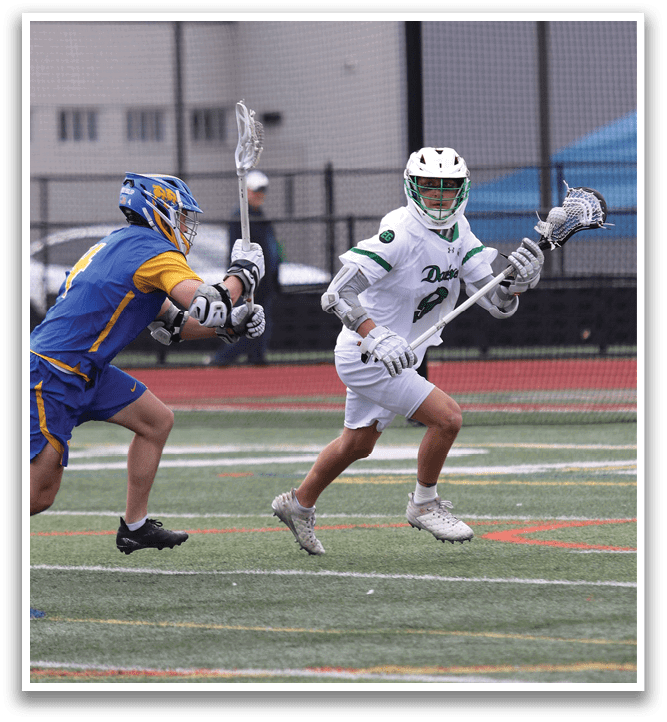A man in a white shirt and green shorts is holding a lacrosse stick. Description generated by AI