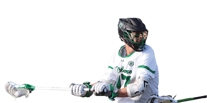 A person wearing a helmet and sports uniform is playing lacrosse on a field while holding a lacrosse stick. Description generated by AI