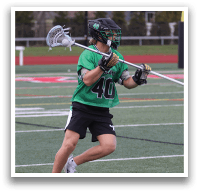 A man in a green shirt and black shorts is holding a lacrosse stick. Description generated by AI
