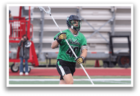 A man wearing a green shirt and black shorts is holding a lacrosse stick. Description generated by AI