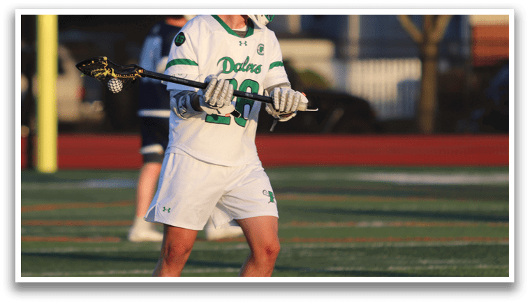 A man wearing a white shirt and white shorts is holding a lacrosse stick. Description generated by AI