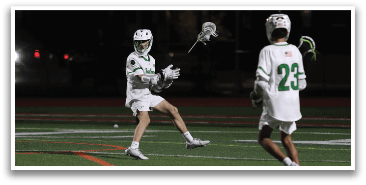 Two men playing lacrosse on a field. Description generated by AI