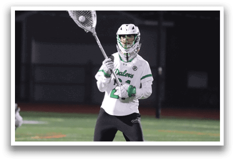 A man in a white and green uniform holding a lacrosse stick. Description generated by AI