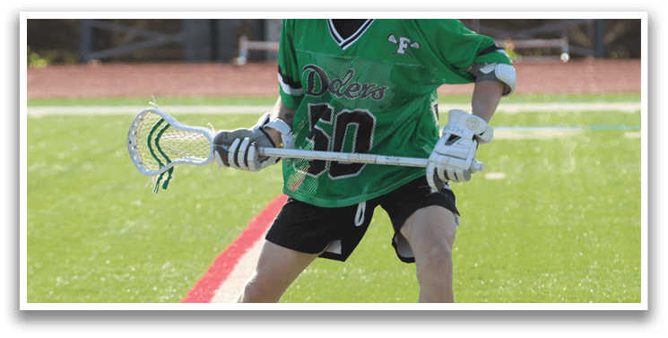 A man wearing a green shirt and shorts holding a lacrosse stick. Description generated by AI