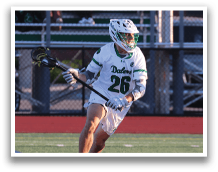 A man wearing a green and white uniform is playing lacrosse. Description generated by AI