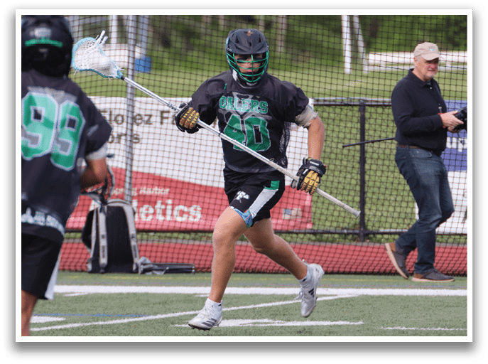 A man wearing a black and green jersey is holding a lacrosse stick. Description generated by AI