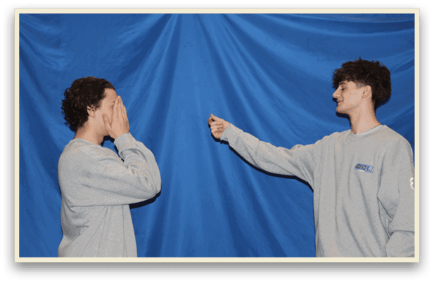 Two people standing in front of a blue curtain. One person is pointing at the other. AI generated content