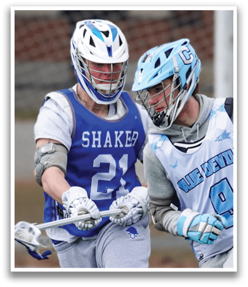 Two men playing lacrosse on a field. One man is wearing a blue and white uniform and is holding a lacrosse stick. The other man is wearing a gray uniform and is attempting to block the first man's shot. AI generated content