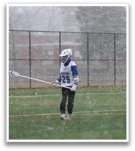 A person wearing a blue and white uniform is holding a lacrosse stick and standing on a field. AI generated content