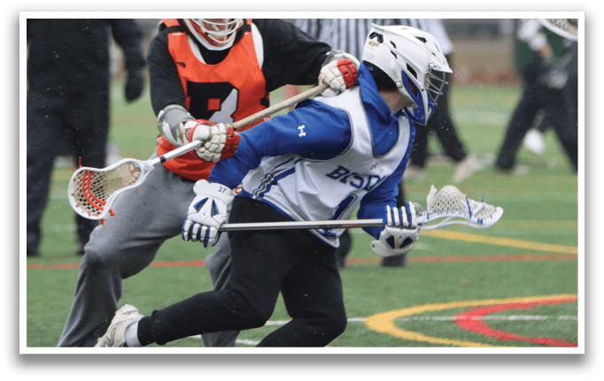 Two men are playing lacrosse on a field. One man is wearing an orange jersey and the other is wearing a blue jersey. They are both holding lacrosse sticks and are in the middle of a play. AI generated content
